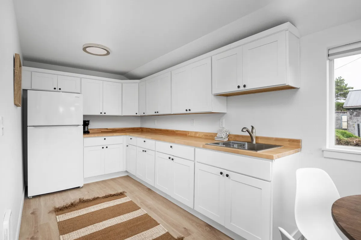 This modern, fresh kitchen scene features white cabinetry, a wooden countertop, a sink, and a window with soft light. The surfaces are clean and contemporary, and the entire space is designed for easy care and durability, making it ideal for relaxed stays and family meals.