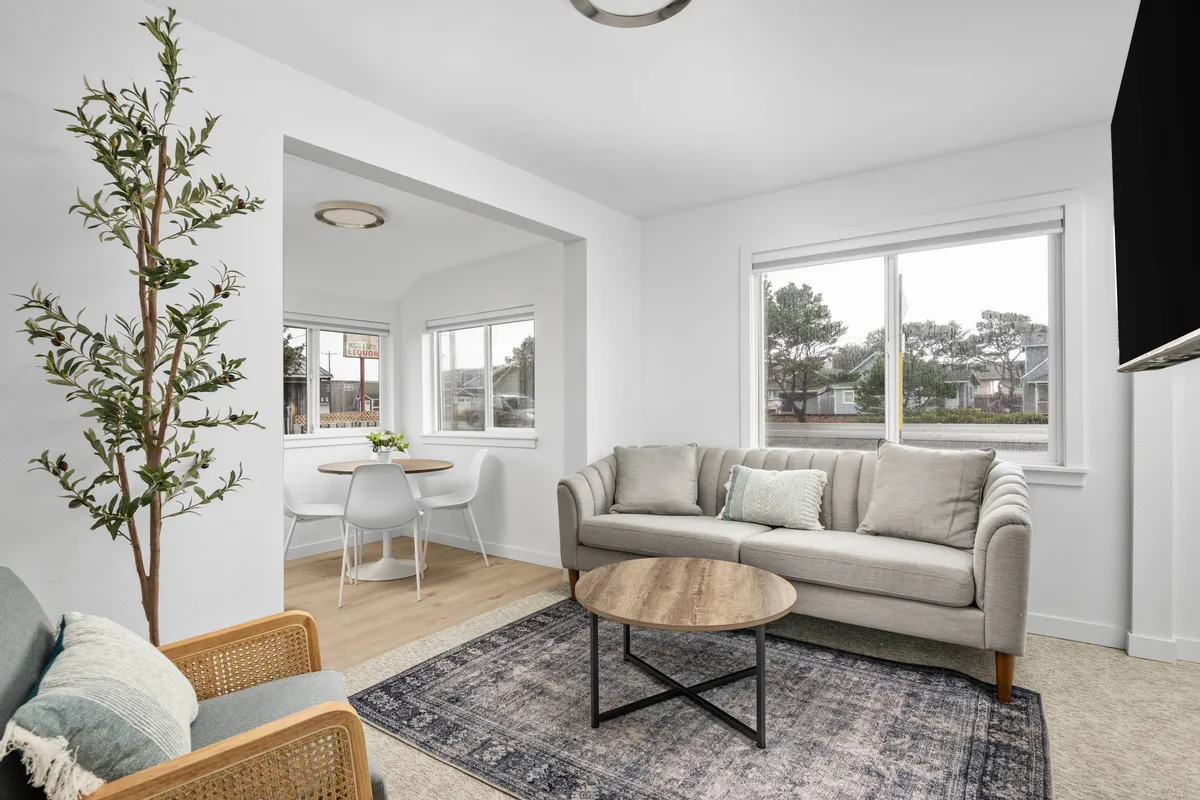 The photo showcases a bright, inviting living space in the condo: a plush sofa faces a stylish coffee table, with a decorative plant adding a touch of greenery. Sunlight pours through wide windows, illuminating the open dining area, ideal for shared meals and relaxing moments. The décor is modern yet cozy, emphasizing comfort and style.