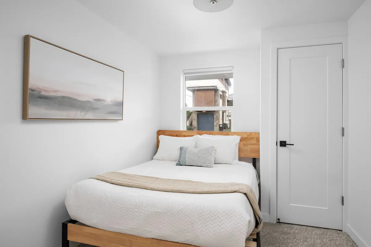 A tranquil bedroom scene featuring a plush bed dressed in soft linens, with tasteful artwork on the wall and a window letting in gentle natural light. The space feels serene and welcoming, ideal for unwinding after a busy day.