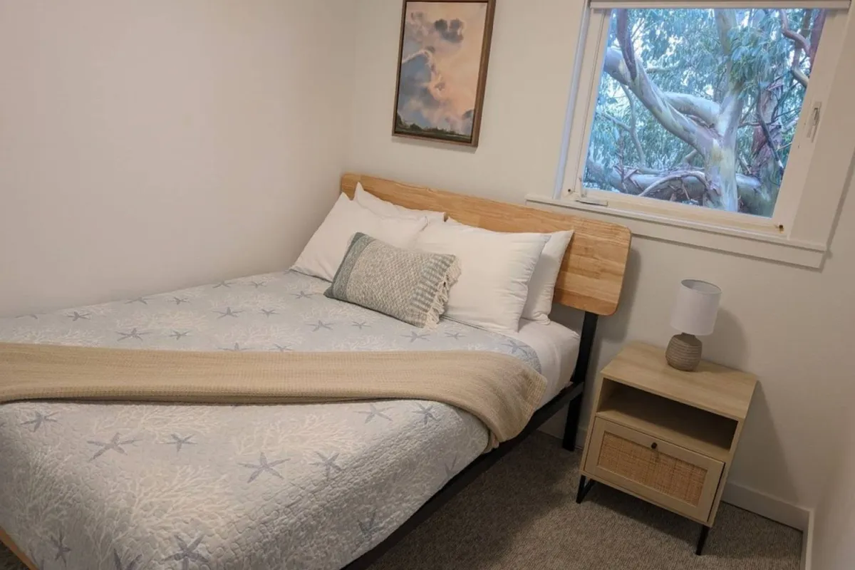 A cozy bedroom with a comfortable bed, a nightstand, and decorative artwork. The window offers a view of nature, and the room exudes a relaxing ambiance, ideal for both quiet nights and gentle mornings.