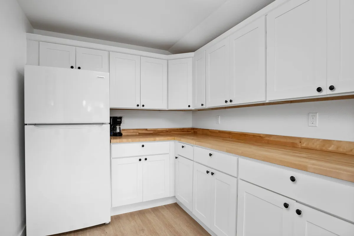 This image features a functional kitchenette area with a white refrigerator, wooden countertop, and cabinetry. The space feels inviting and practical, designed for easy meal preparation and informal social gatherings.